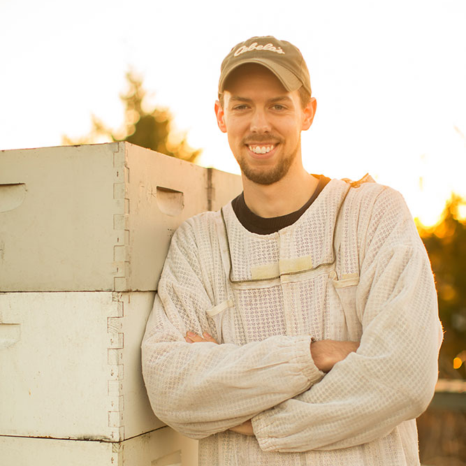 beekeeping in a protective suit standing next to a stack of beehives. 